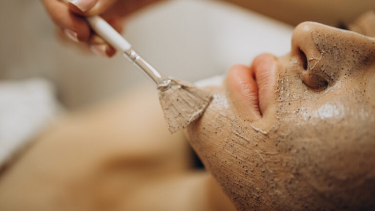 Woman visiting cosmetologist, applying rejuvenation face scrub