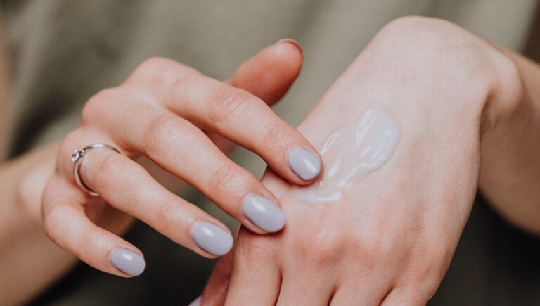 a woman showing a anti-aging serum on her hand. the background in blurry and is of sage color