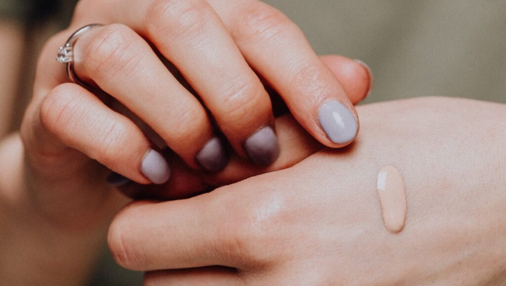 cracked up makeup foundation dropping on a woman's hand, while she's trying to touch it