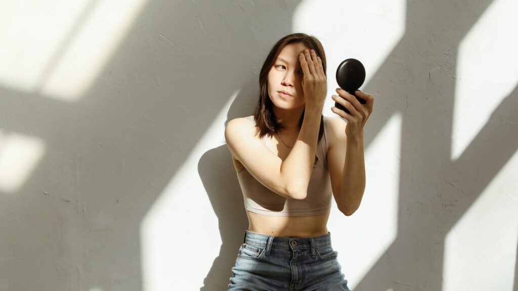 woman applying Watery foundation with a sponge leaning against a wall