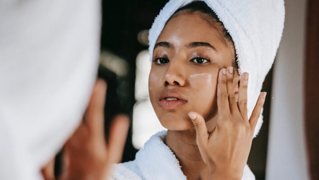 an afro woman applying moisturizer for acne-prone skin