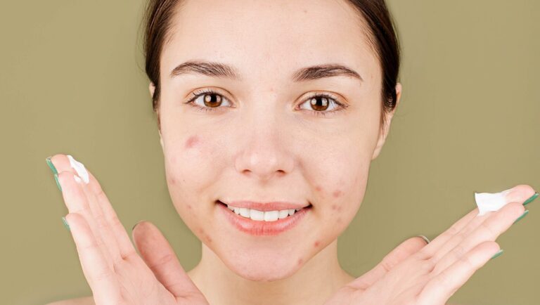 woman holding concealer in fingers as she smiles for the camera.