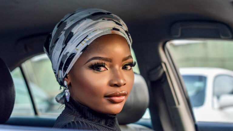 an afro woman sitting in car looking into the camera as she wears magnetic eyelashes