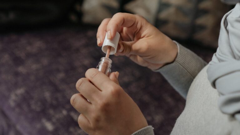 woman in grey clothes holding a clear lip gloss with both of her hands