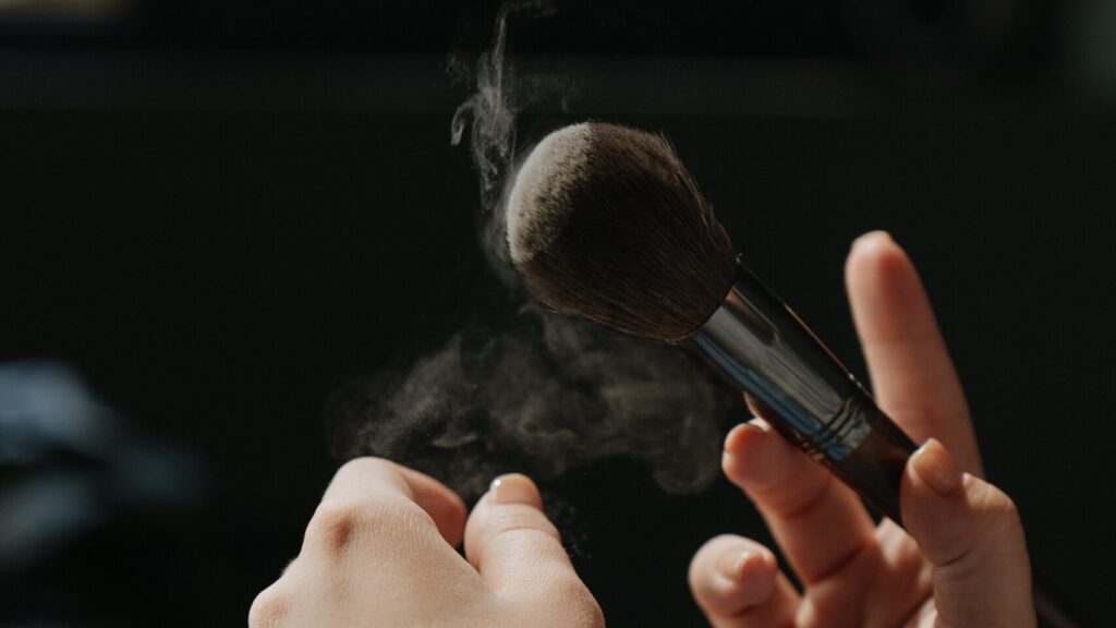 two hands dusting the makeup powder off a brush