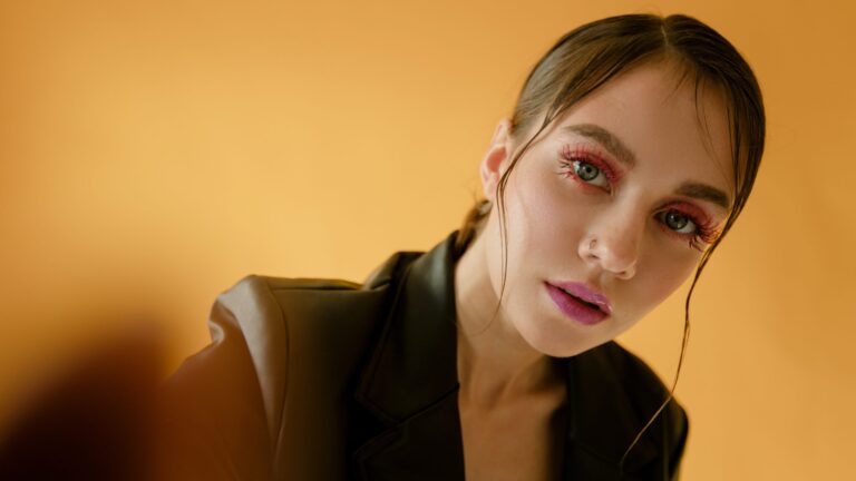 a woman posing for a photo in front og a yellow background as she has brown eyeshadow and coral lipstick on