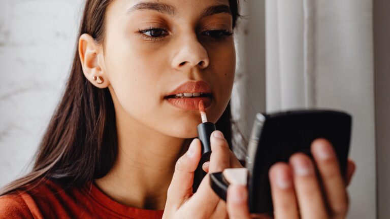 a woman applying red lop gloss looking into the mirror