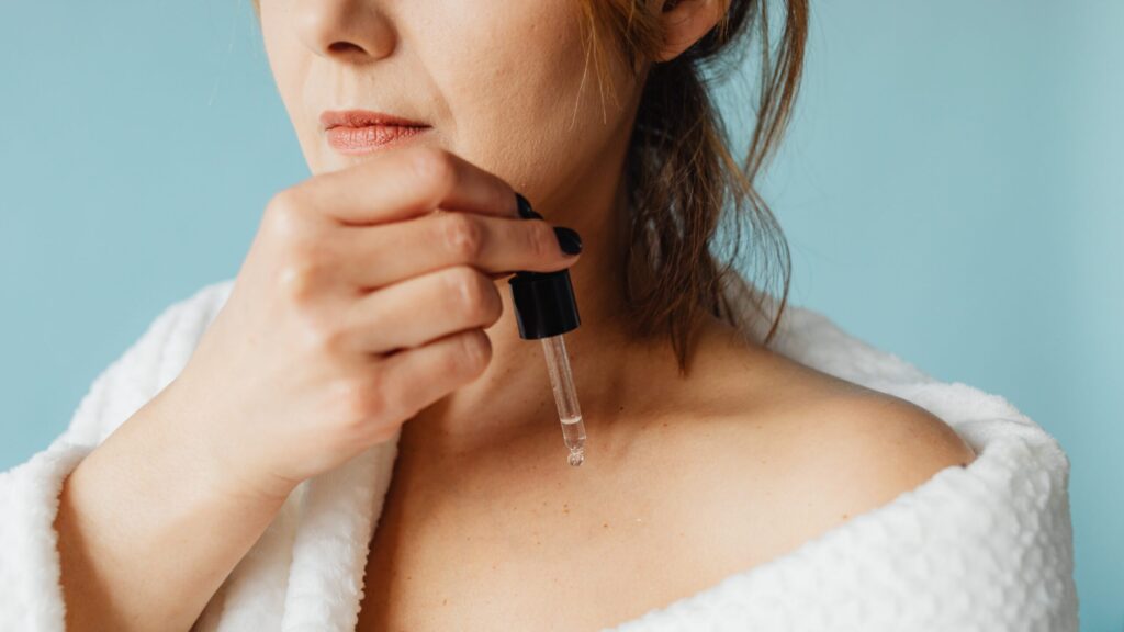 woman in white robe pouring serum with a dripper on her body.