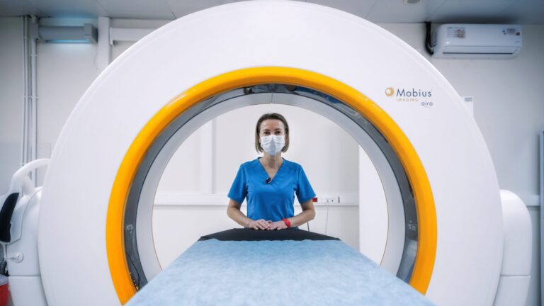 shot of a nurse in blue scrub from the opposite side of an MRI machine