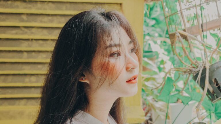a Chinese woman sitting on her patio looing into the looks as she has blush on and has used her lip gloss as a blush