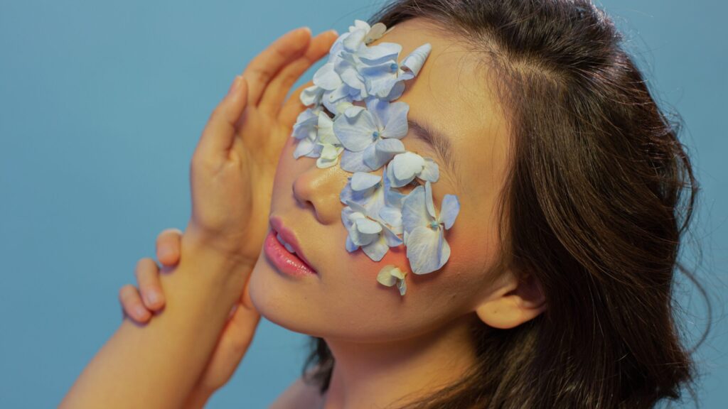 a woman with flowers on her eyes posing in front of camera as she has lip gloss on