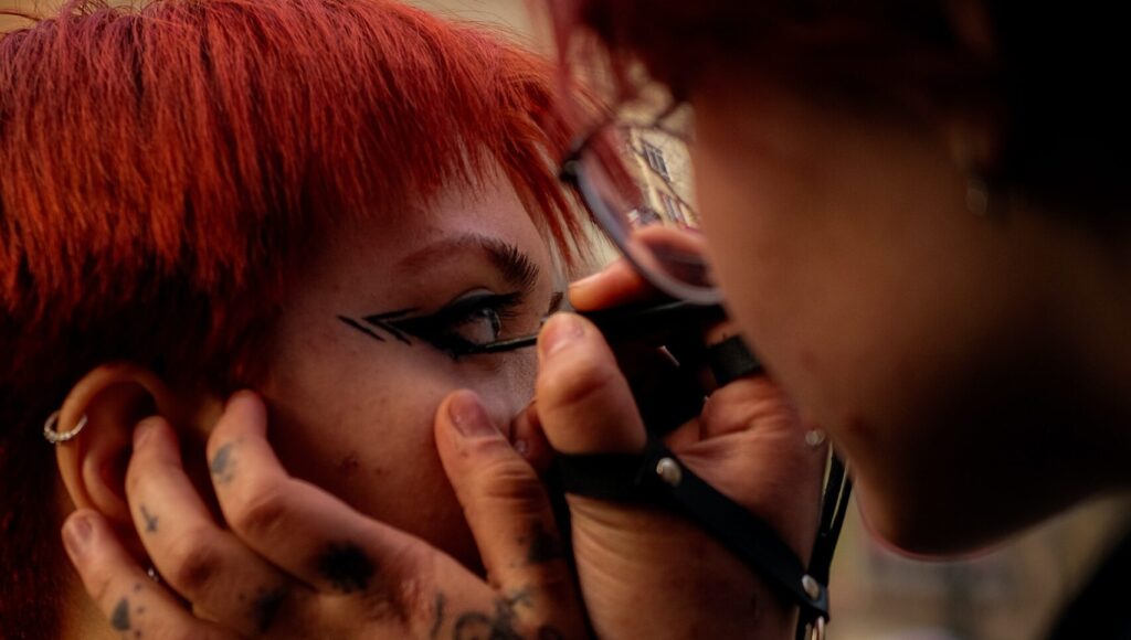 a man with tattoos on his hand applying eyeliner on a woman with eyelash extensions