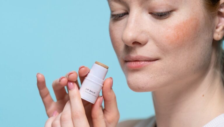 woman holding a concealer bottle in her hands as she poses in front of a blue background