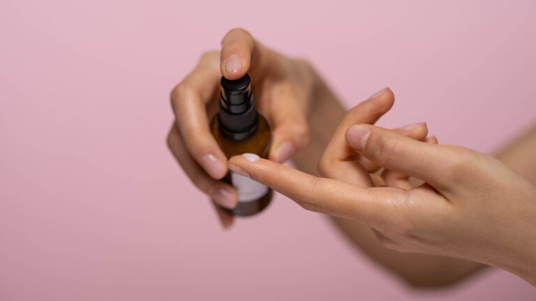 two hands pouring collagen serum in front of a pink background