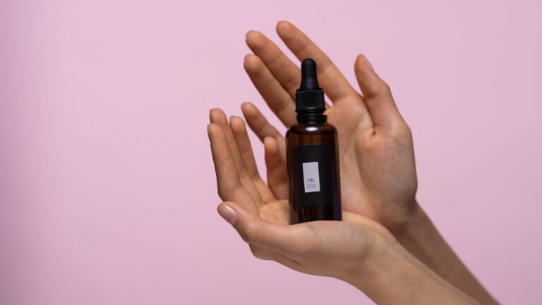 two hands holding collagen serum bottle in front of a pink a background