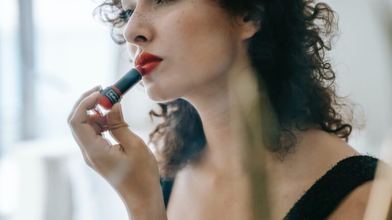 a woman applying red lip gloss as she is wearing a black shirt