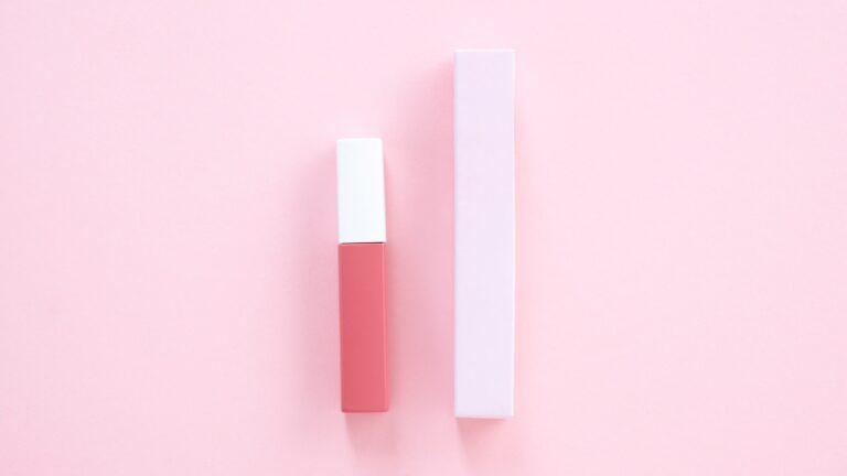 a lip gloss and its box placed on a pink background