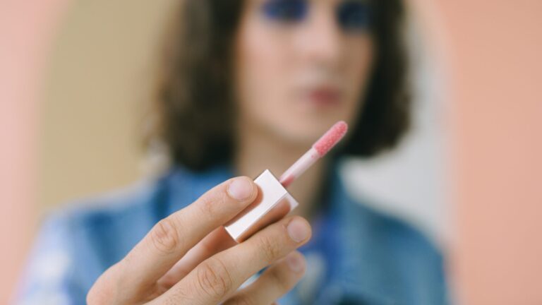 a focused photo of a lip gloss brush as a woman stands in the background holding it