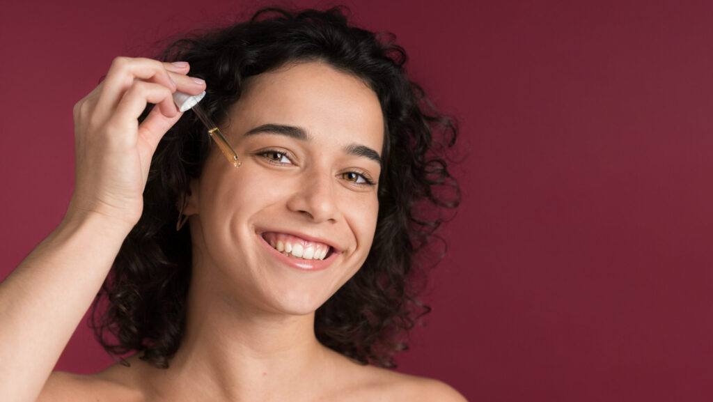 woman pouring mineral-based seum on her face with a dripper as she smiles for the camera