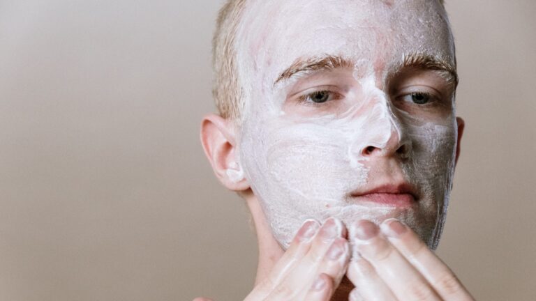 a man's close up as he is rubbing toothpaste on his face with his hands for acne treatment