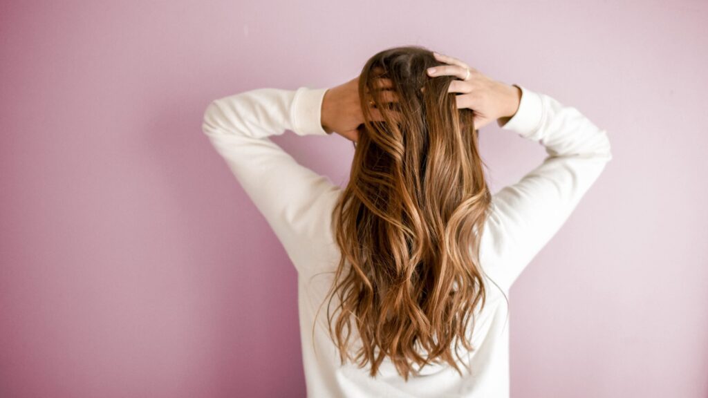 a woman's back as she runs her fingers through her hair standing in front of a pink background