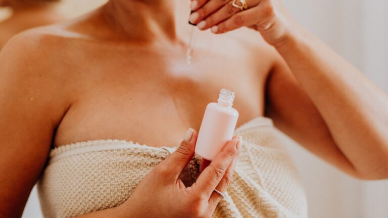 a woman's body as she is wearing a white towel around her naval, she applies anti-aging face serum on her body with a dripper which she made at home