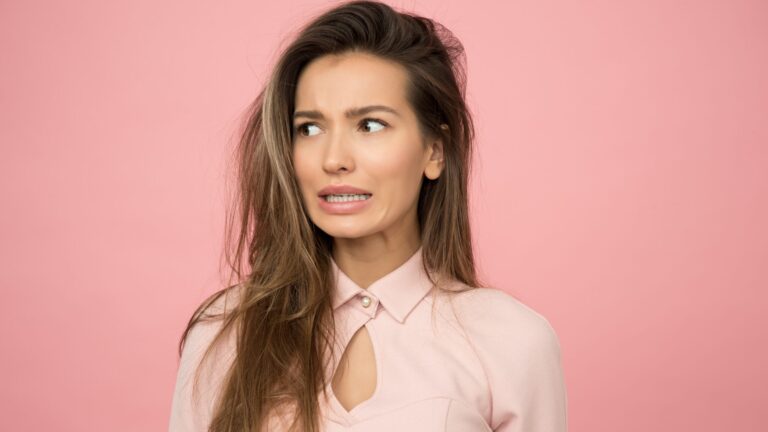 a woman worrying about her oily scalp as she wears pink colored clothes and stands in front a pink background