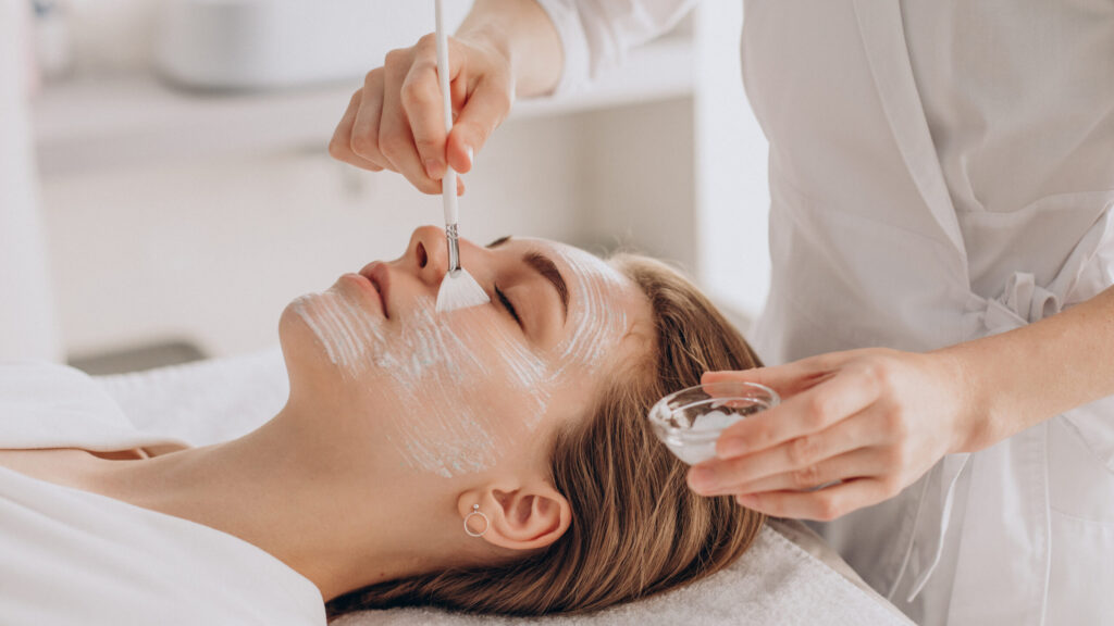 a woman getting a mast put on her face as a step in hydra facial as she lies down on a bed