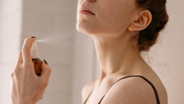 woman wearing a black tank-top spraying herself with rosewater which is in a black container.