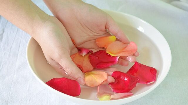 woman having her hands dipped in rose water as she's trying to pick up rose petals from the rosewater