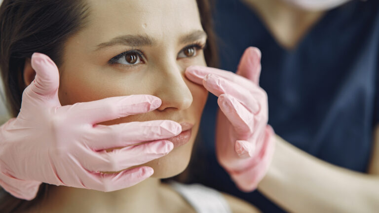 a surgeon checking a woman's under eyes with their pink gloves after under-eye fillers