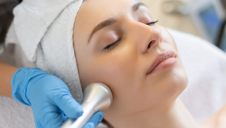 a woman getting a HydraFacial treatment as she lies down wearing a white towel on her head