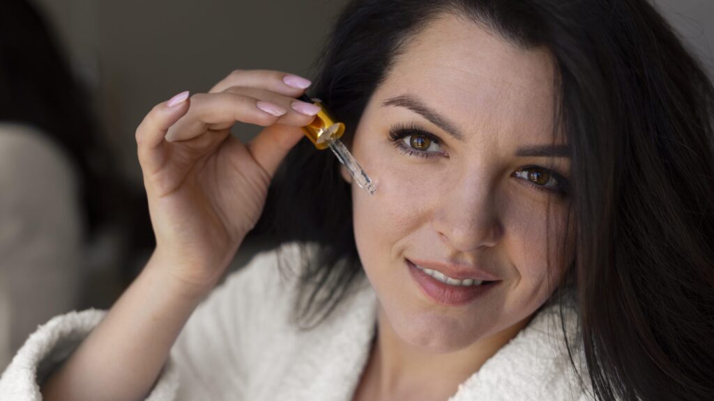 a lady wearing a white towel robe dropping gold serum on her face