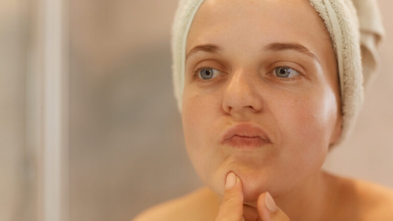 Closeup portrait of beautiful woman looking at her face, trying find acne, posing with naked shoulders and towel over head, after doing hydrafacial