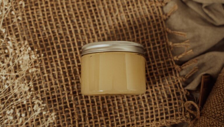 a glass bottle of turmeric face scrub with a silver lead placed on a jute fabric.