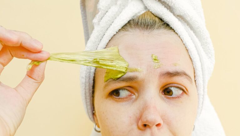 woman with white towel on her head peeling off turmeric mask from her forehead.