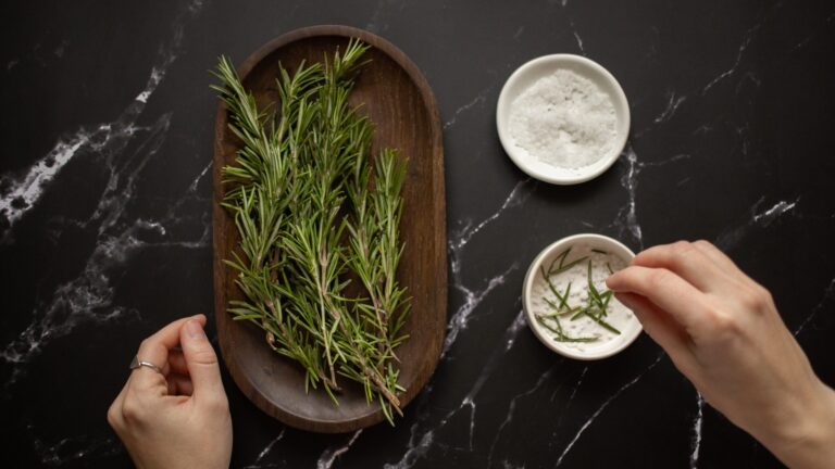 a tray of rosemary besides two bowls on salt scrub, one having a mixture of herbs