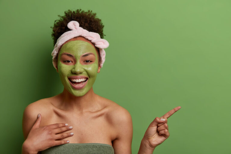 woman standing in front of a green background with a green mask on her face