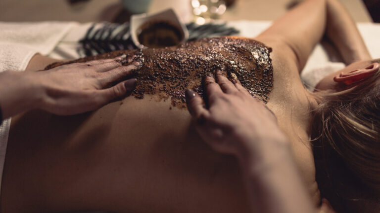 a woman getting body scrub on her back by two afro hands