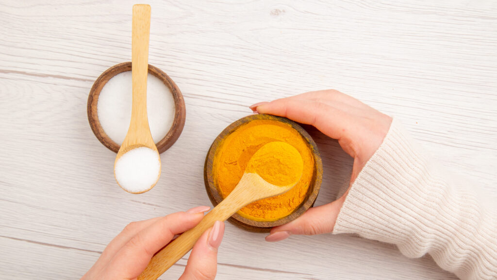 woman holding Turmeric Face Scrub in a bowl. besides another bowl with yogurt and a spoon in it