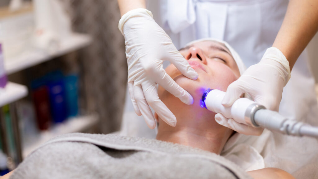 A young beautiful girl lies on the beautician's table and receives hydrafacial with a professional apparatus for skin rejuvenation and moisturizing.